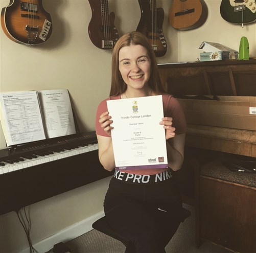 A photo of a joyful girl proudly displaying her Grade 6 piano certificate